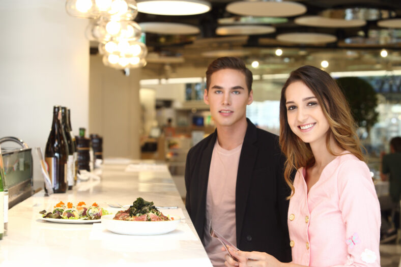 Un par de amantes de la moda que cenan en el restaurante Fusion Handsome Man Black Jacket Aduana hermosa mujer con un vestido de moda sentado en el café moderno que habla la fecha de la fecha del almuerzo, el espacio de copia, la mujer focal blur hombre