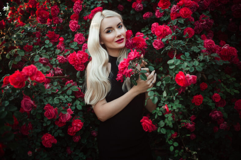 Beautiful smiling blonde woman in bush of red roses