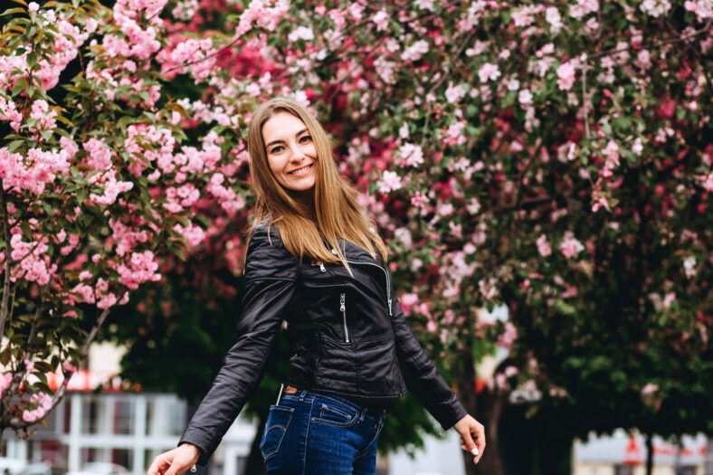 Outdoor portrait of young beautiful fashionable lady posing near flowering tree. Female beauty fashion. City lifestyle. girl in yellow cardigan on a background of pink flowering trees. Girl smiling
