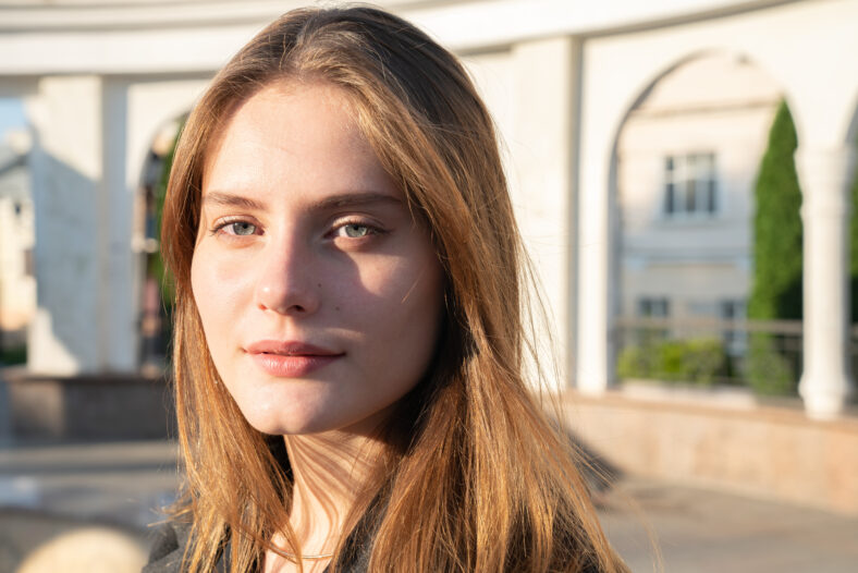 Close up portrait of the beautiful serious girl with brunette loose hair and red lips, summer sunny day
