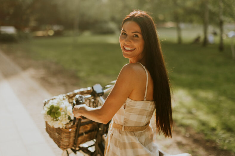 Pretty young woman with flowers in the basket of electric bike