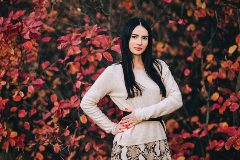 Portrait, photo of a beautiful girl, brunette woman in autumn against the background of red bushes with leaves.