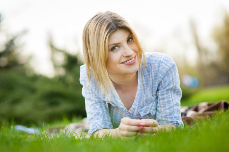 Horizontal portrait of a beautiful woman laying in the grass with a smile on her face