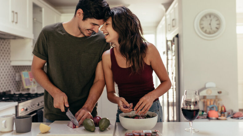 Loving young couple cutting vegetables together at kitchen counter. Young man and woman in love cooking food together at home.