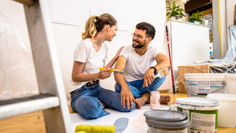 Young couple sitting on the floor choosing color for painting the wall in their home.
