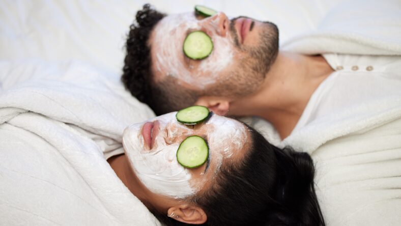 Facial, spa and relax with couple and mask for skincare, cosmetics and detox treatment. Beauty, face and self care weekend with man and woman in bedroom at home for salon, wellness and cucumber.