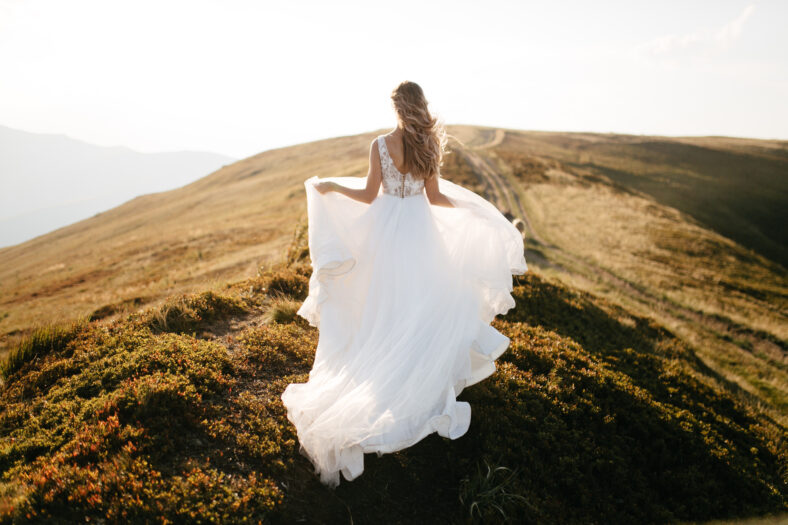 Stylish bride standing on beautiful landscape of mountains on sunset