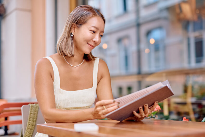 Young woman reading menu at outdoor cafe in summer