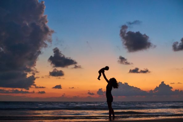 silhouette of mother carrying child in front of beautiful ocean beach sunset
