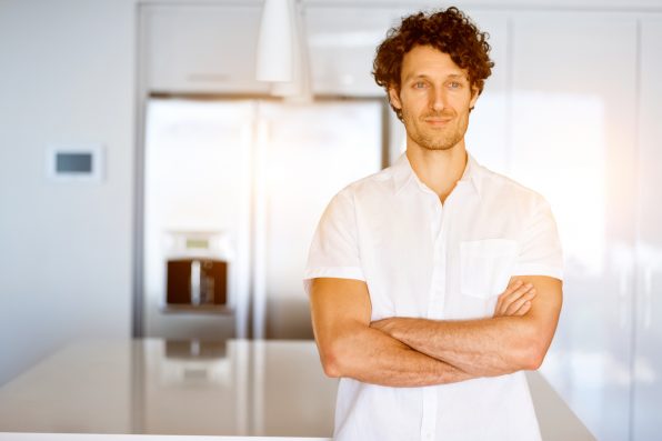 Portrait of a smart young man with curly hair standing in kitchen