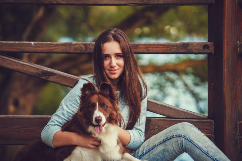 Young woman playing with collie dog outdoors in the park.