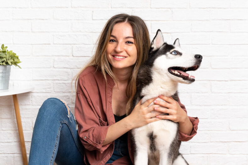 Young pretty woman with her husky dog sitting in the floor at indoors