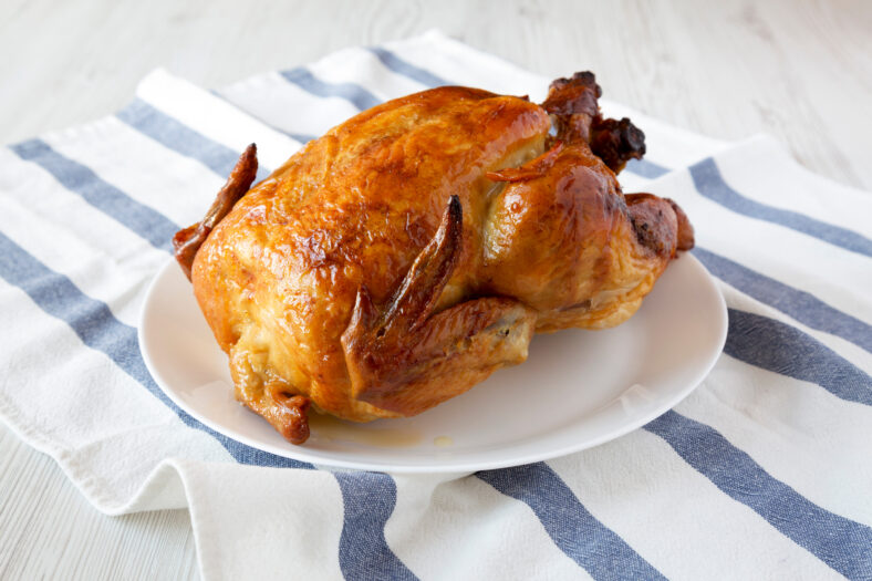 Homemade tasty rotisserie chicken on white plate, side view. Close-up.