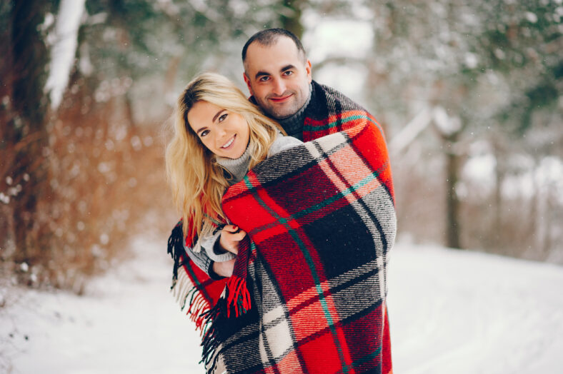 couple walking in a winter park. Man and woman have fun with snow. Pair with red blanket