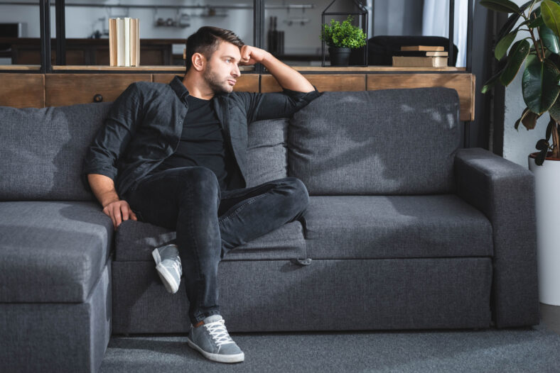 Handsome man sitting on the couch looking sad.