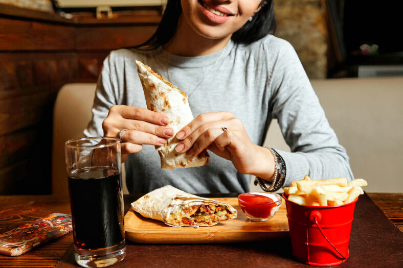 A woman is photographed seated at a table, enjoying a burrito.