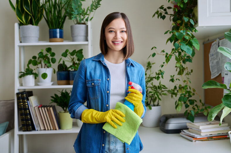 Retrato de casa de limpieza de mujeres jóvenes, con guantes protectores con spray de limpieza mirando la cámara. Limpieza, rutina doméstica, estilo de vida, concepto juvenil