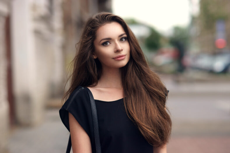Fashion style portrait of young beautiful elegant woman in black dress walking at city streets on a windy dull day.