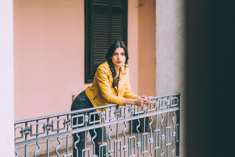 young handsome brown straight hair woman leaning on handrail outdoor in the city using smart phone hand hold looking at camera pensive - technology, communication, social network concept