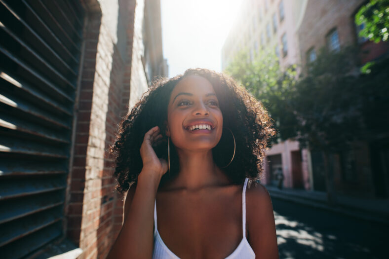 Portrait of beautiful young african woman walking down the city street. Afro american female walking outdoors looking away and smiling