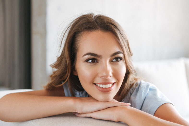 Close up of a smiling young woman relaxing on a couch at home and looking away