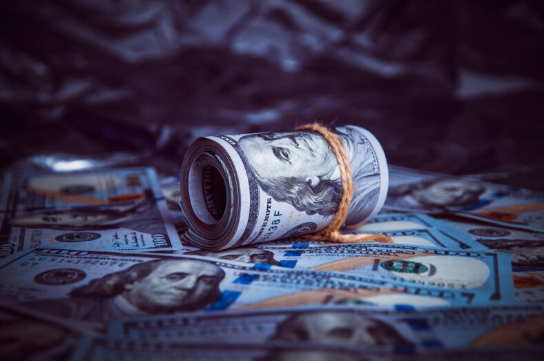 In the dark on broken money is a roll of dollars lit by a ray of light.