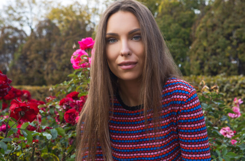 Portrait of beautiful young girl near flower bed of roses.