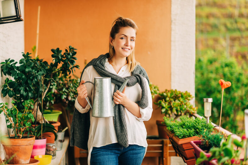 Portrait of beautiful woman watering green plants on the balcony, small cozy garden in apartment