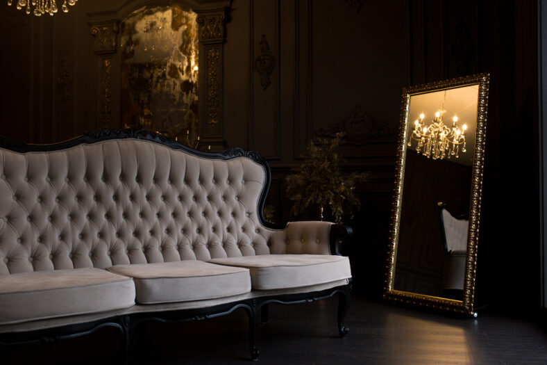 Ancient beige sofa in a dark room with a vintage mirror.