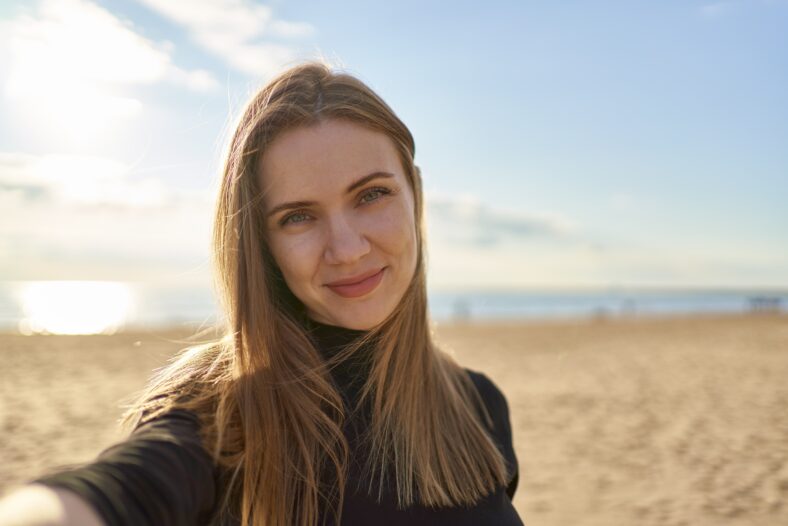 Pretty female with long hair looking at camera and smiling in sunny evening in ocean