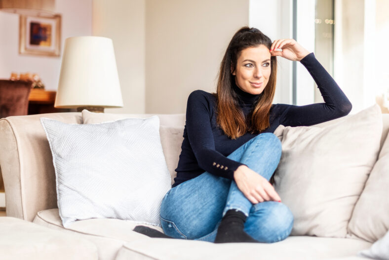 Full length shot of attractive woman wearing casual clothes while relaxing on the sofa at home.