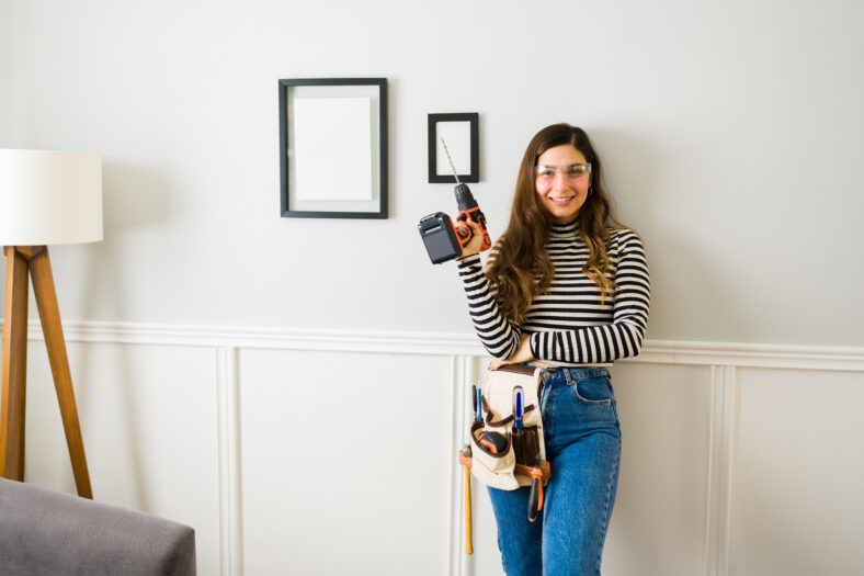 Happy attractive woman making eye contact while using tools and a drill to do home repairs