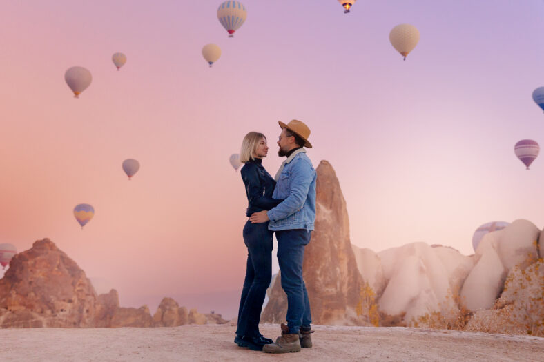 Loving couple hugging against background of hot air colorful balloons, romantic honeymoon in Cappadocia Turkey. Travel photo of man and woman tourist.