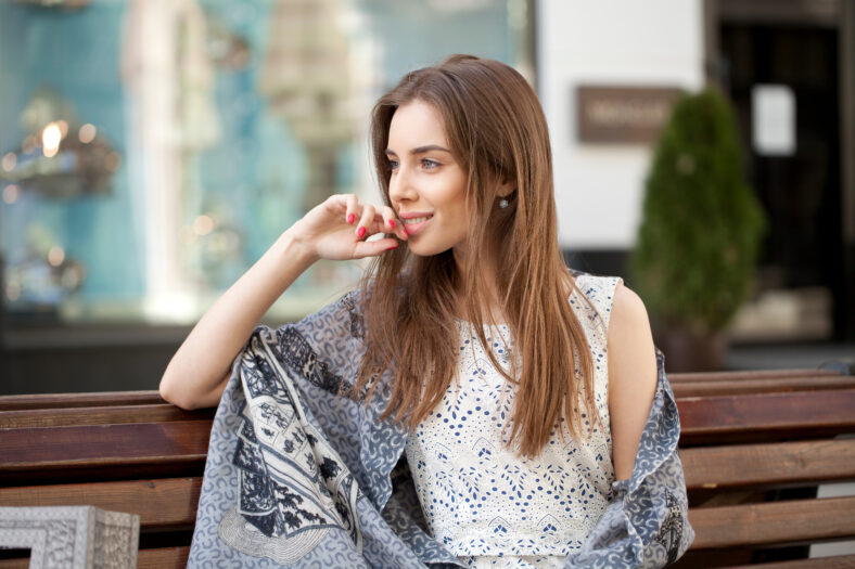 Cute young brunette woman sitting on the bench in summer street