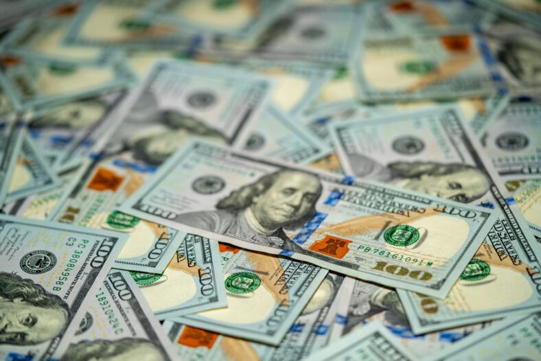 A collection of hundred dollar bills is spread out on a flat surface, showcasing the intricate designs and vibrant colors of the currency in detail.