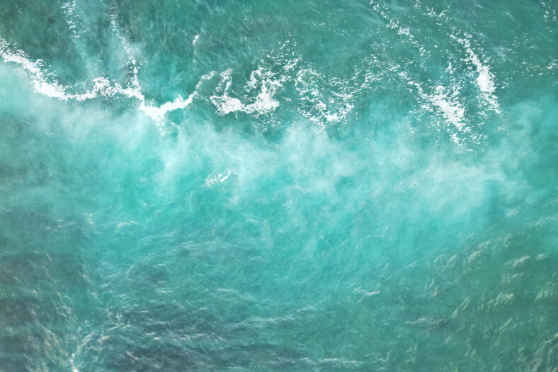 Vista aérea de las ondas del océano turquesa con crestas blancas espumosas que crean un patrón abstracto fascinante en la superficie del agua.