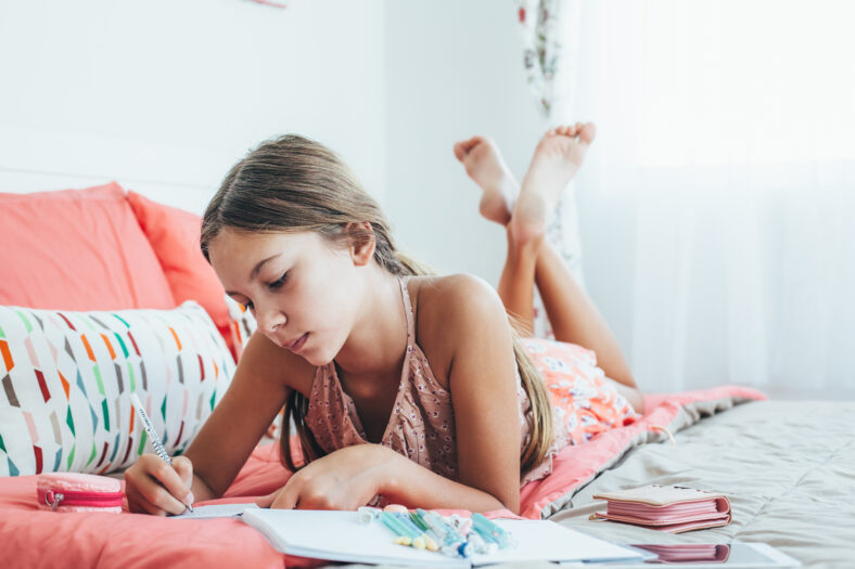 10-12 years old pre teen girl writing diary in pink bedroom