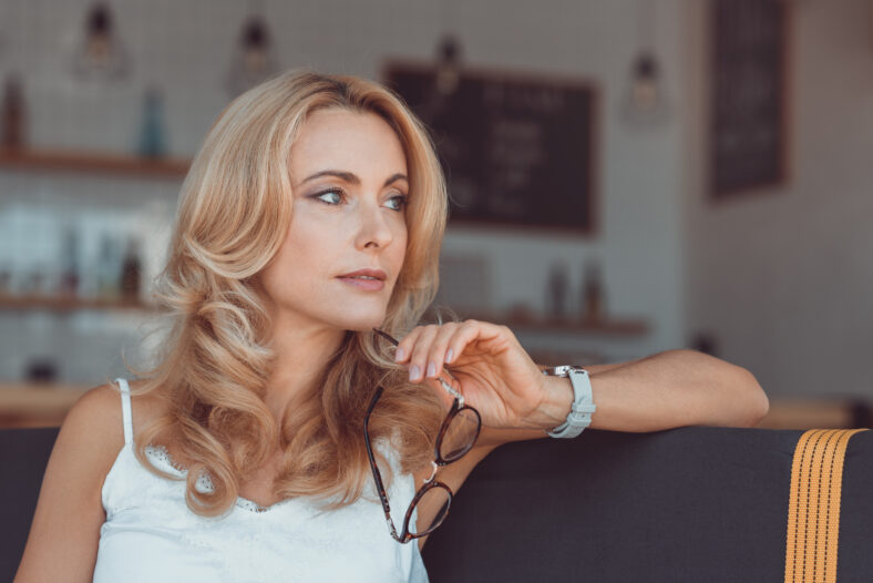 beautiful pensive middle aged woman holding eyeglasses and looking away