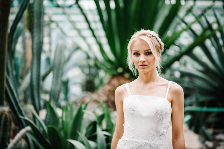 Woman stand in the Botanical green garden full of greenery. Wedding ceremony. Portrait attractive blonde bride standing in a wedding dress on the background of greenery.