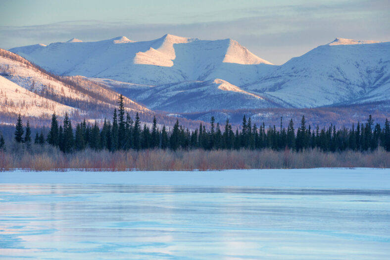 Snowy mountains in the rays of dawn. Winter landscape with the mountains and the frozen lake in Yakutia, Siberia at sunrise. Clear blue ice of the frozen lake at morning Frosty morning, day or evening