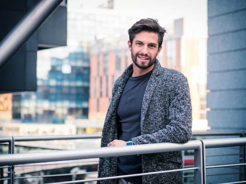 One handsome young man in urban setting in European city, standing and smiling to camera happy