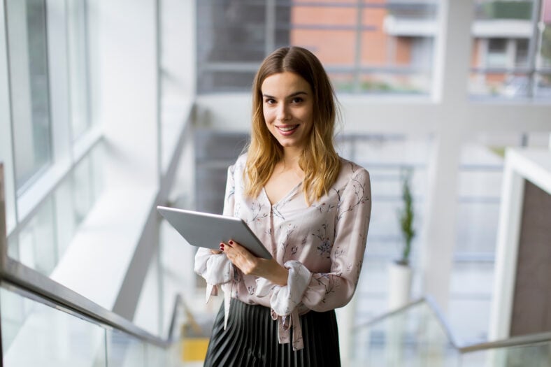 Attractive young businesswoman using a digital tablet while standing on the stairs in the office
