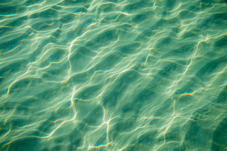 Tropical blue-green waters background in shallow seas with small waves in bright sunlight