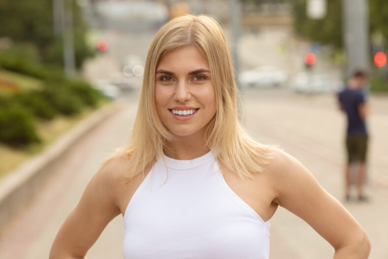 Outdoors lifestyle fashion portrait of happy stunning blonde girl. Beautiful smile. Walking to the city street. Long light hair. Joyful and cheerful woman. Happiness.