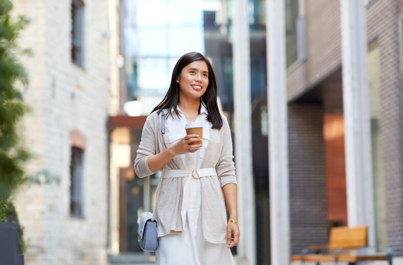 lifestyle and people concept - happy smiling young asian woman with takeaway coffee cup walking along city street
