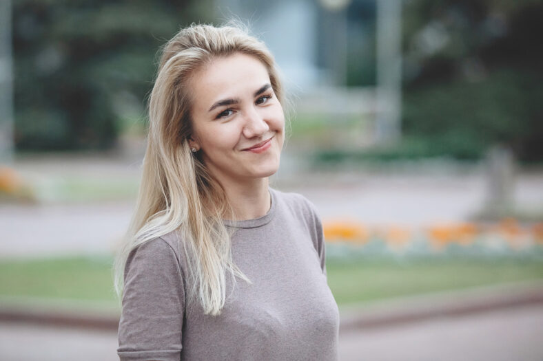 Young pretty blonde woman smiles and looking at the camera outdoors.