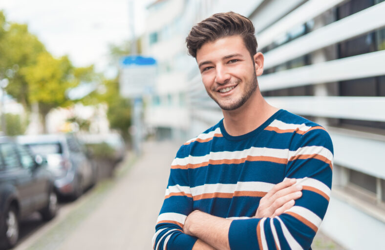 Waist up happy young man smiling to camera in the city, outdoor - outside