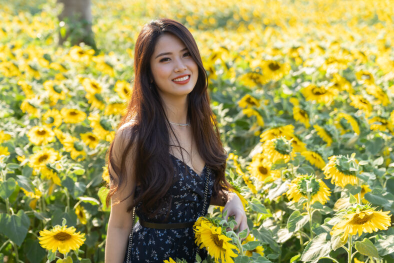 Cheerful multiracial Asian cute young woman joyful, smiling with sunflowers background. Happy carefree summer beautiful girl in sunflower field in spring.