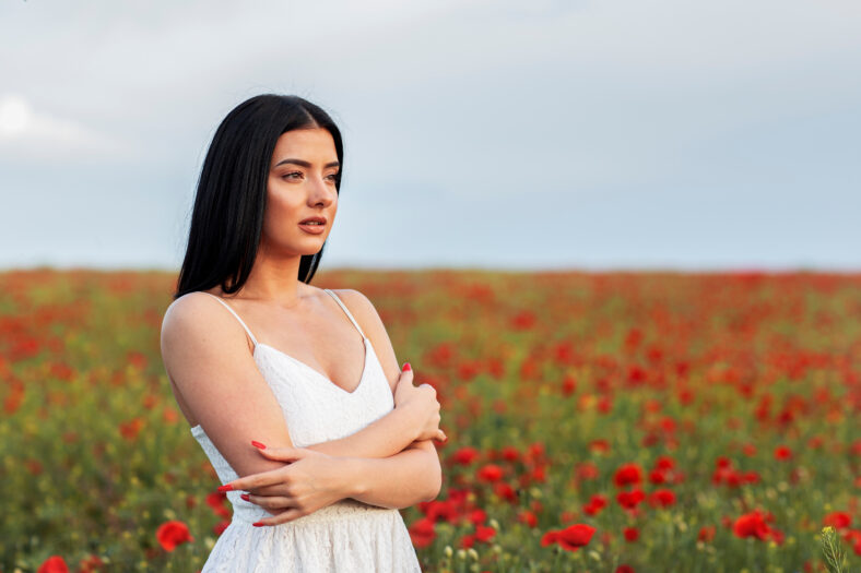 Fashion long black hair woman at the middle of the red flowers field posing