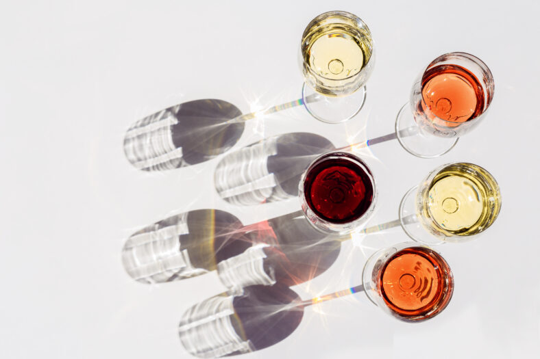 Red, rose and white wine top view in sunlight. Assorted wine in glass on white table. Dark shadows. Bar, winery, wine degustation concept.
